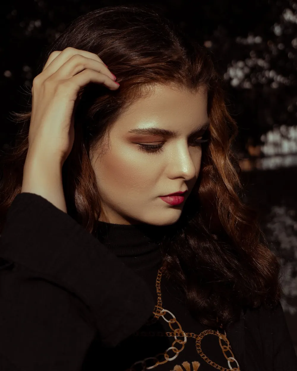 Portrait of a brunette woman with elegant makeup, looking down in thoughtful manner.