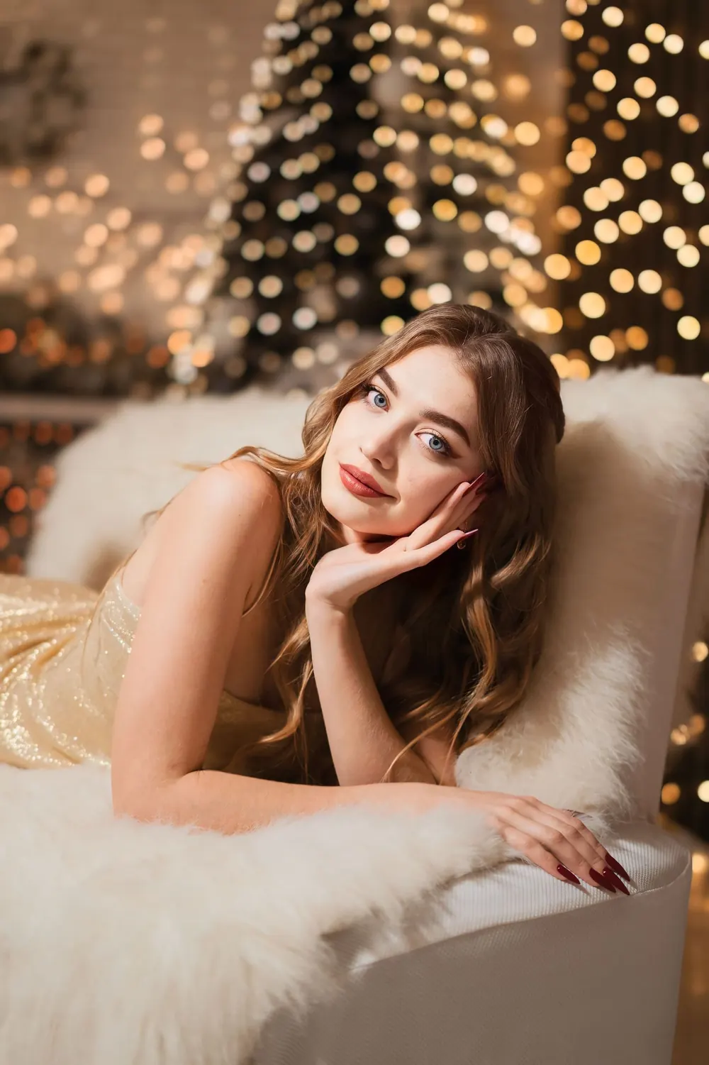 Elegant young woman in a shimmering dress relaxing in a festive, warm glow setting.