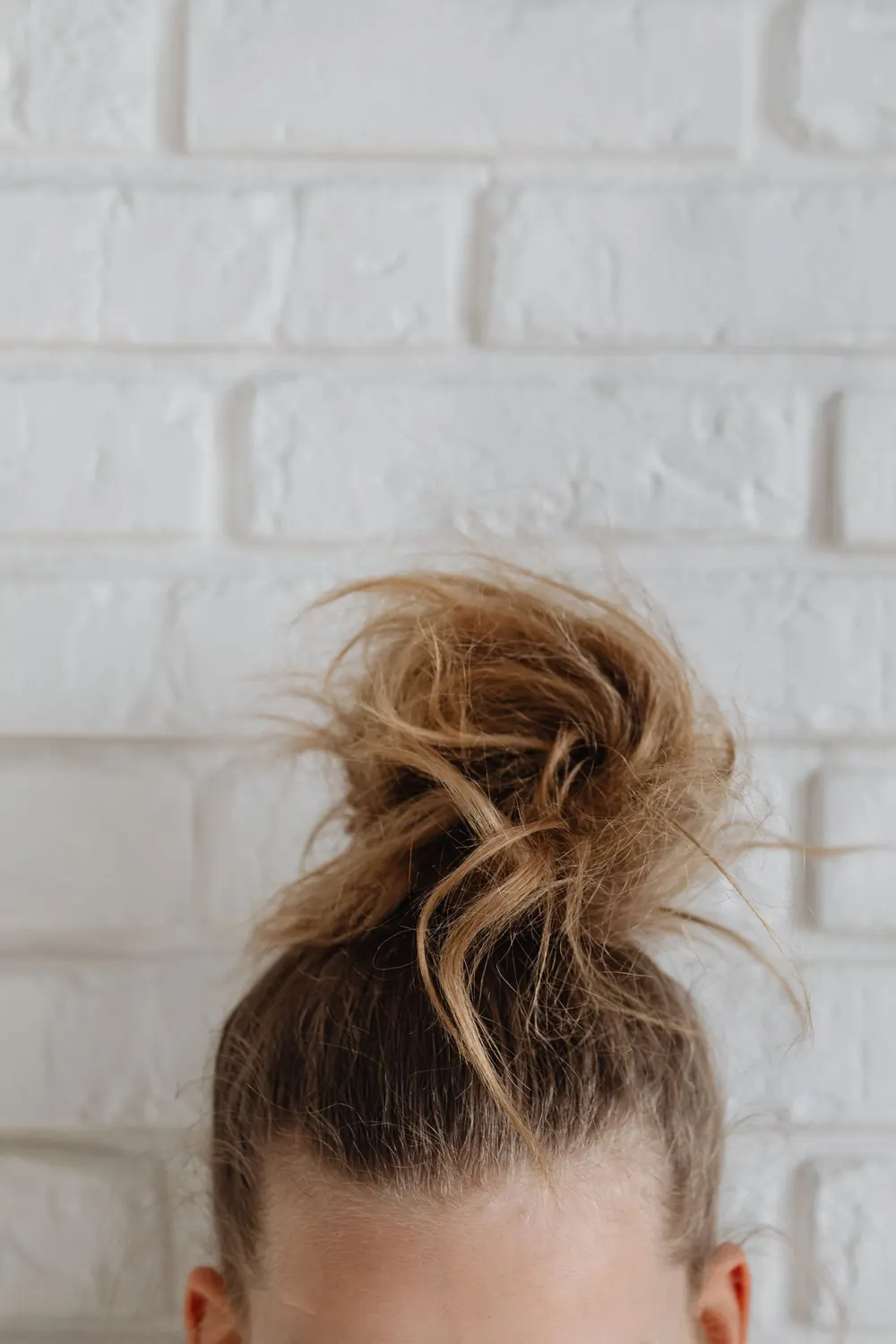Close-up of a messy hair bun styled against a white brick wall for a casual look.