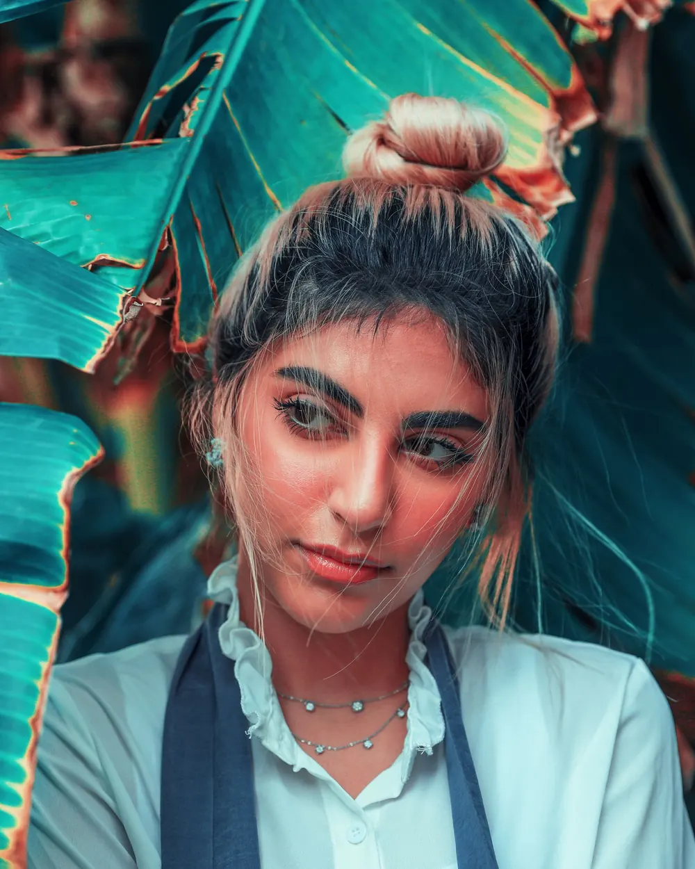 Portrait of a young woman with an elegant style set against a vibrant banana leaf background.