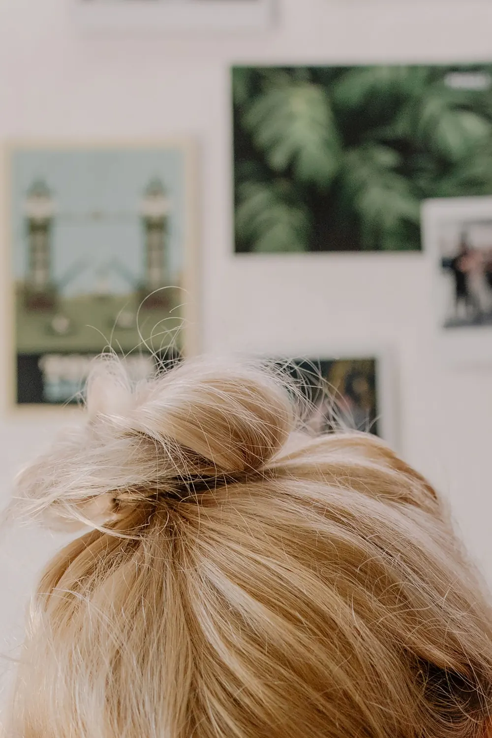 Close-up of a blonde bun hairstyle with modern art posters in the background.