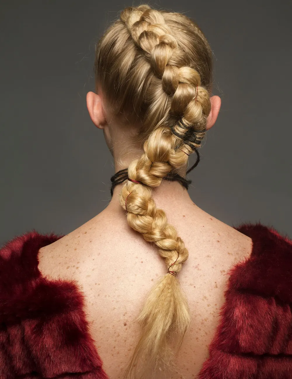 A studio shot capturing a blonde woman's intricate braided hairstyle in a red outfit.