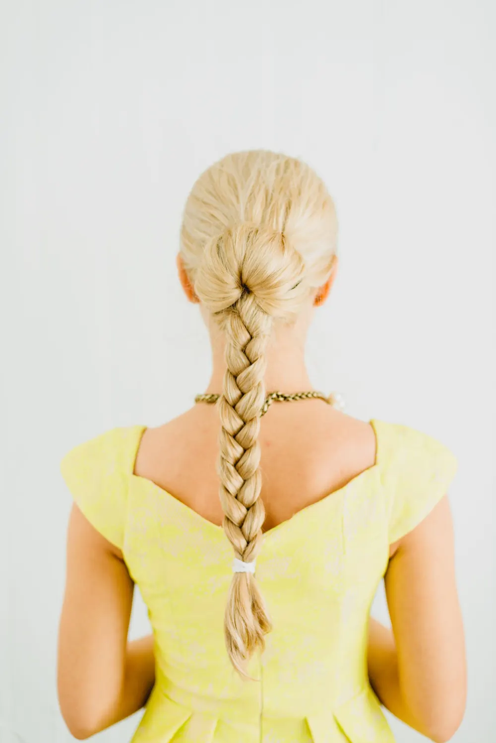 Stylish view of a blonde woman's braid in a yellow dress photographed from behind.