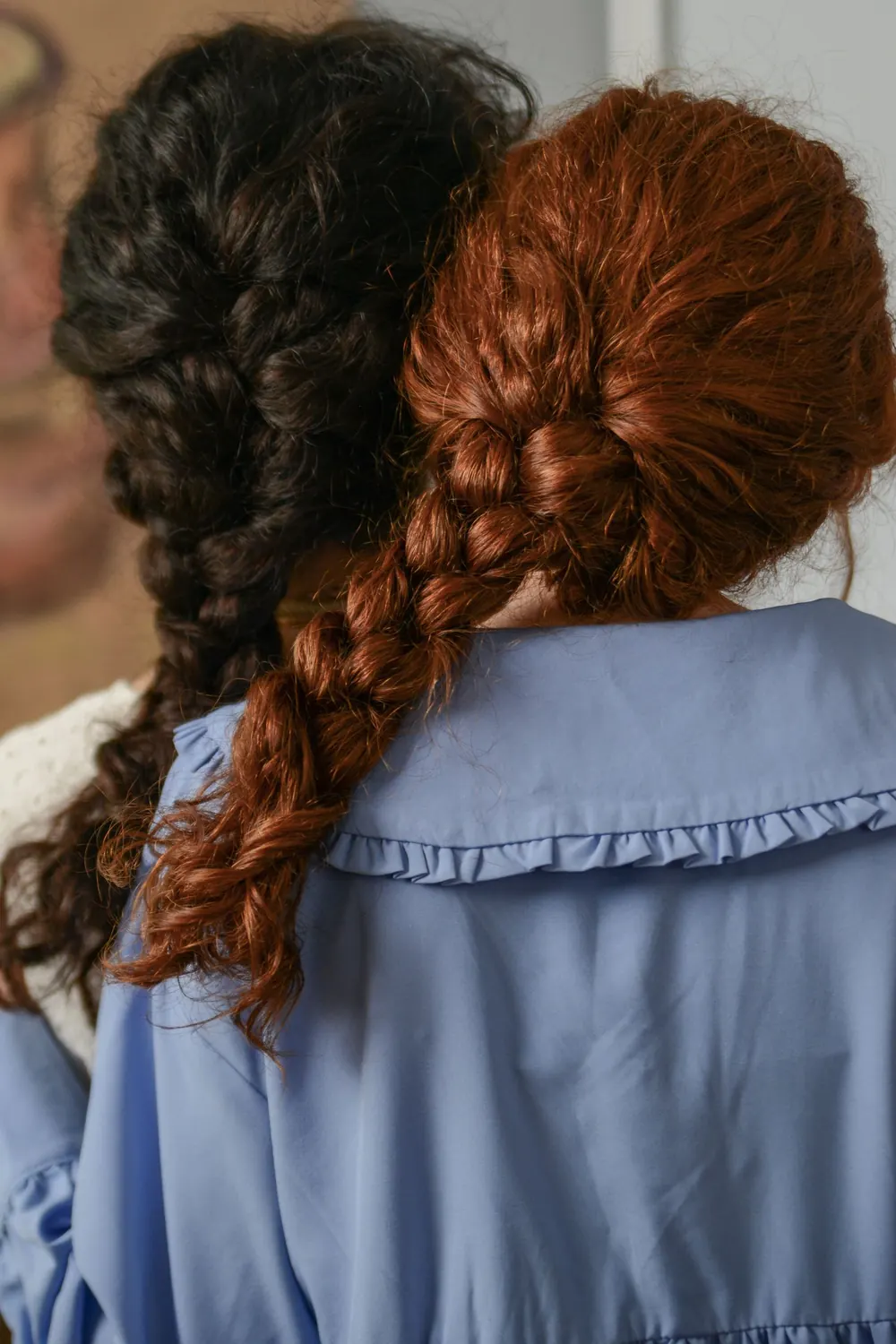 Two women with braided hairstyles, captured from the back, showcasing diverse hair textures indoors.