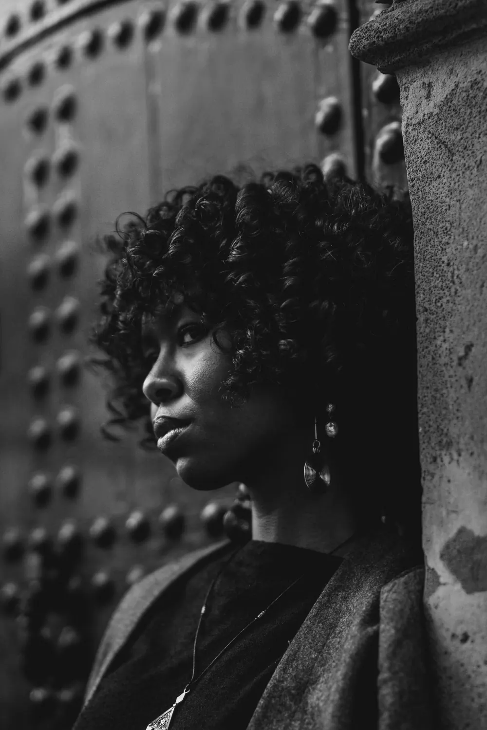 Stylish black and white portrait of a young woman with curly hair leaning against a textured wall.