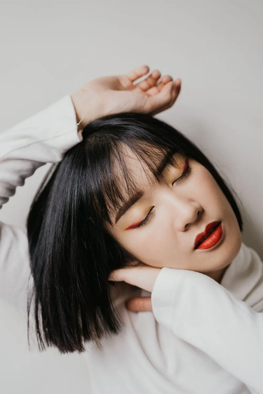 Close-up portrait of a woman with eyes closed and hands on head, serene and elegant.