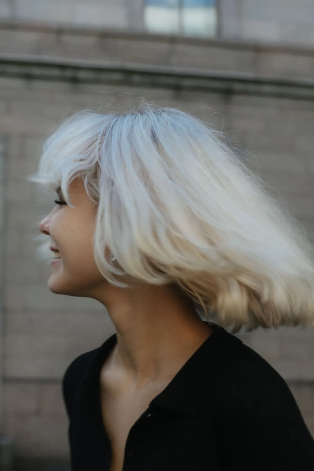A woman with platinum blonde hair smiles outdoors, showcasing happiness and vibrant youth.