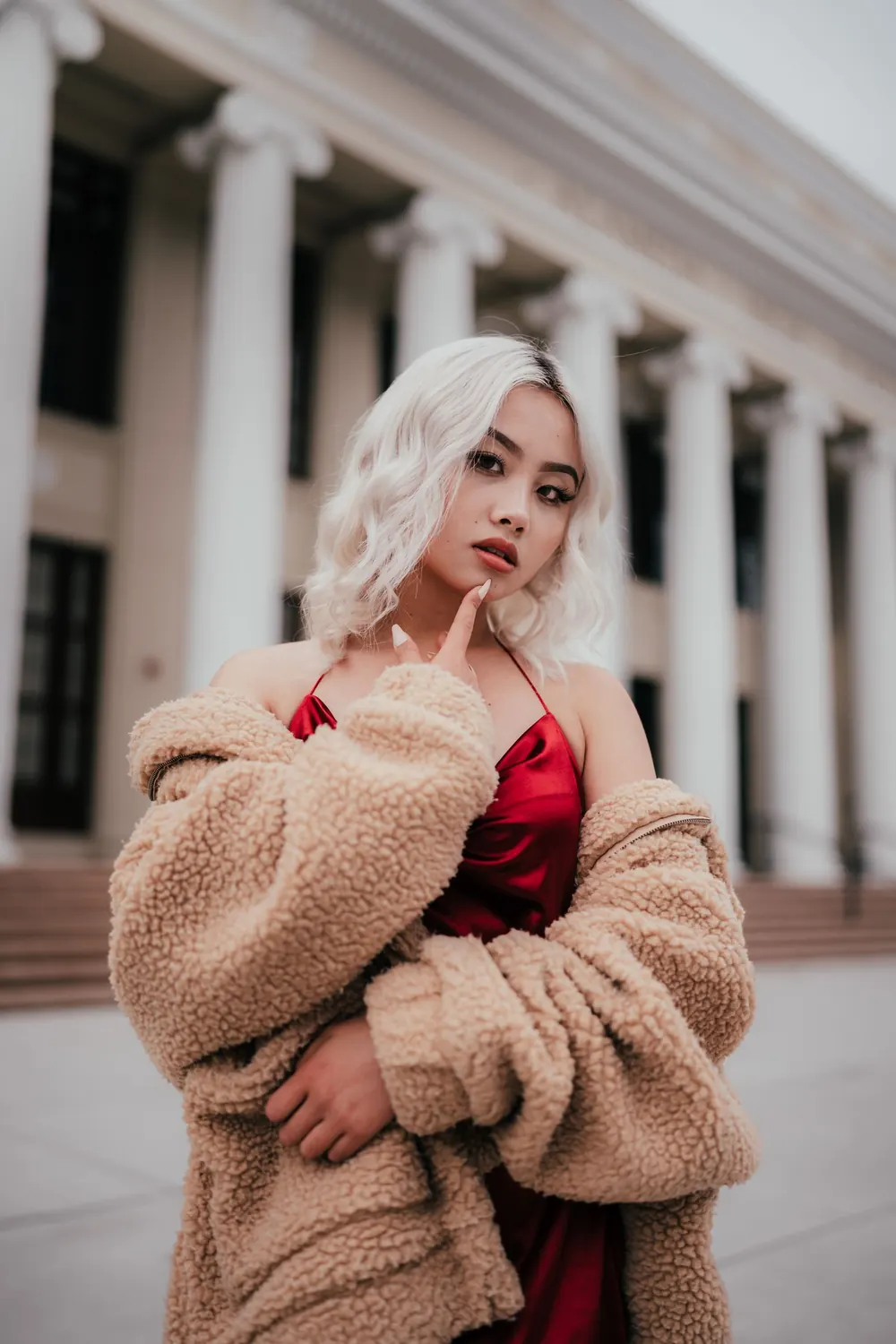 Beautiful woman in red silk dress posing confidently outdoors with a historic building backdrop.