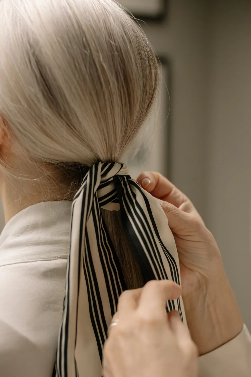 Close-up shot of white hair being styled with a striped scarf, showcasing elegance.