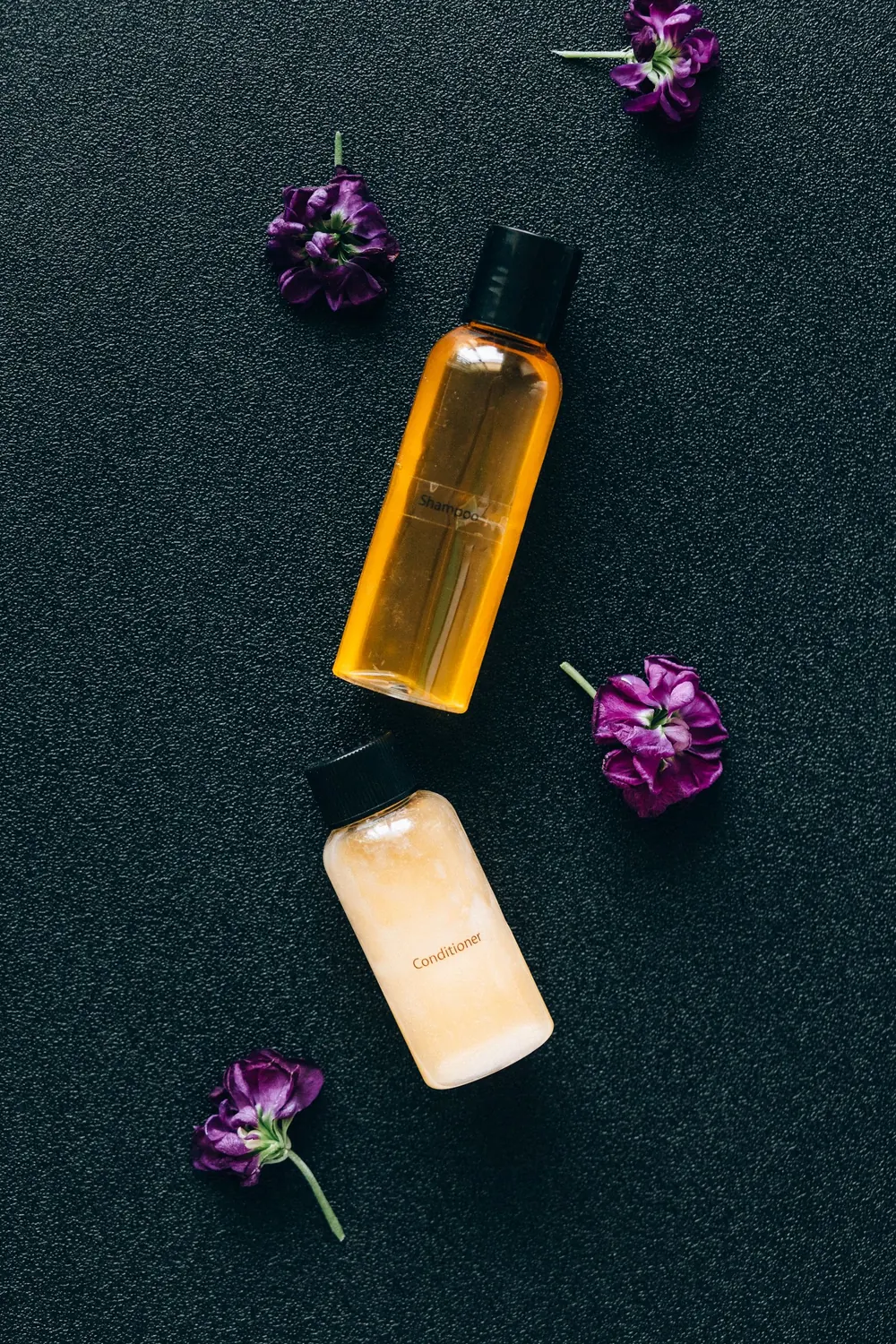 Top view of cosmetic bottles with purple flowers on a textured surface, creating a stylish composition.
