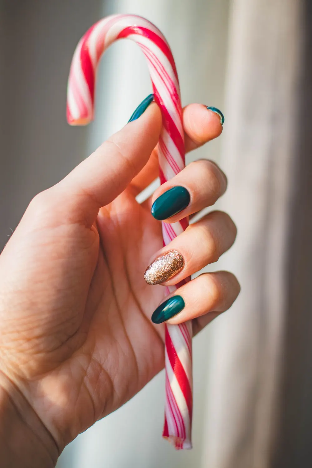 Close-up of a woman's hand holding a candy cane, featuring stylish and festive nail art.