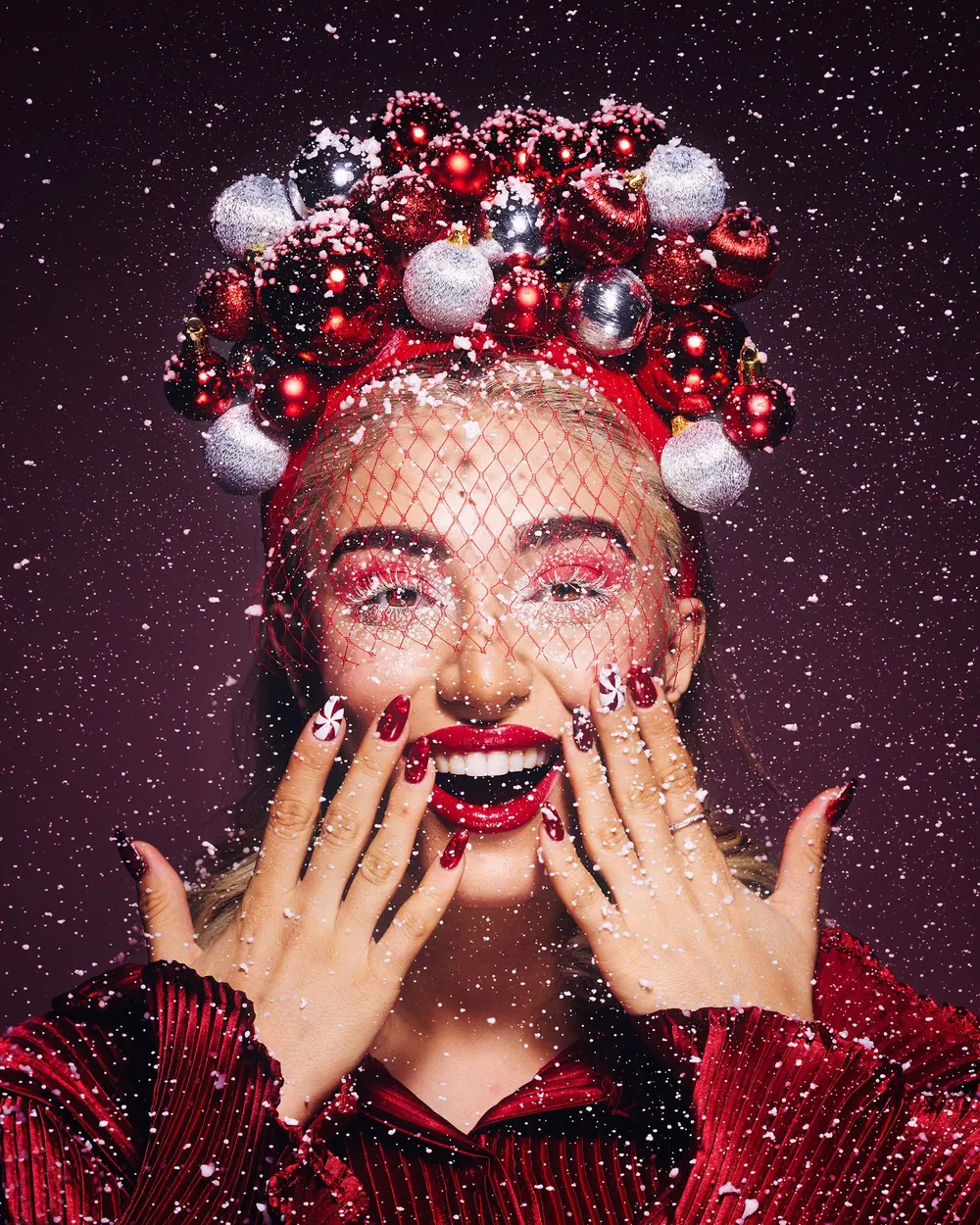 Joyful woman with red and silver ornaments in holiday-themed portrait.